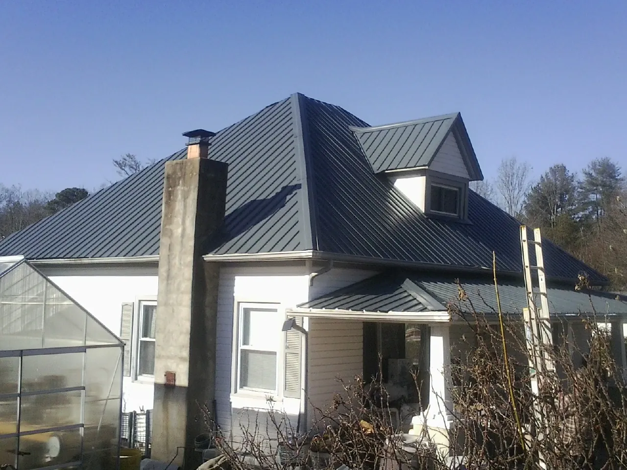 Dark blue standing seam metal roof on a white farmhouse with dormer — Slate & Tile Roof Repair by Roofing Brothers in Saint James City