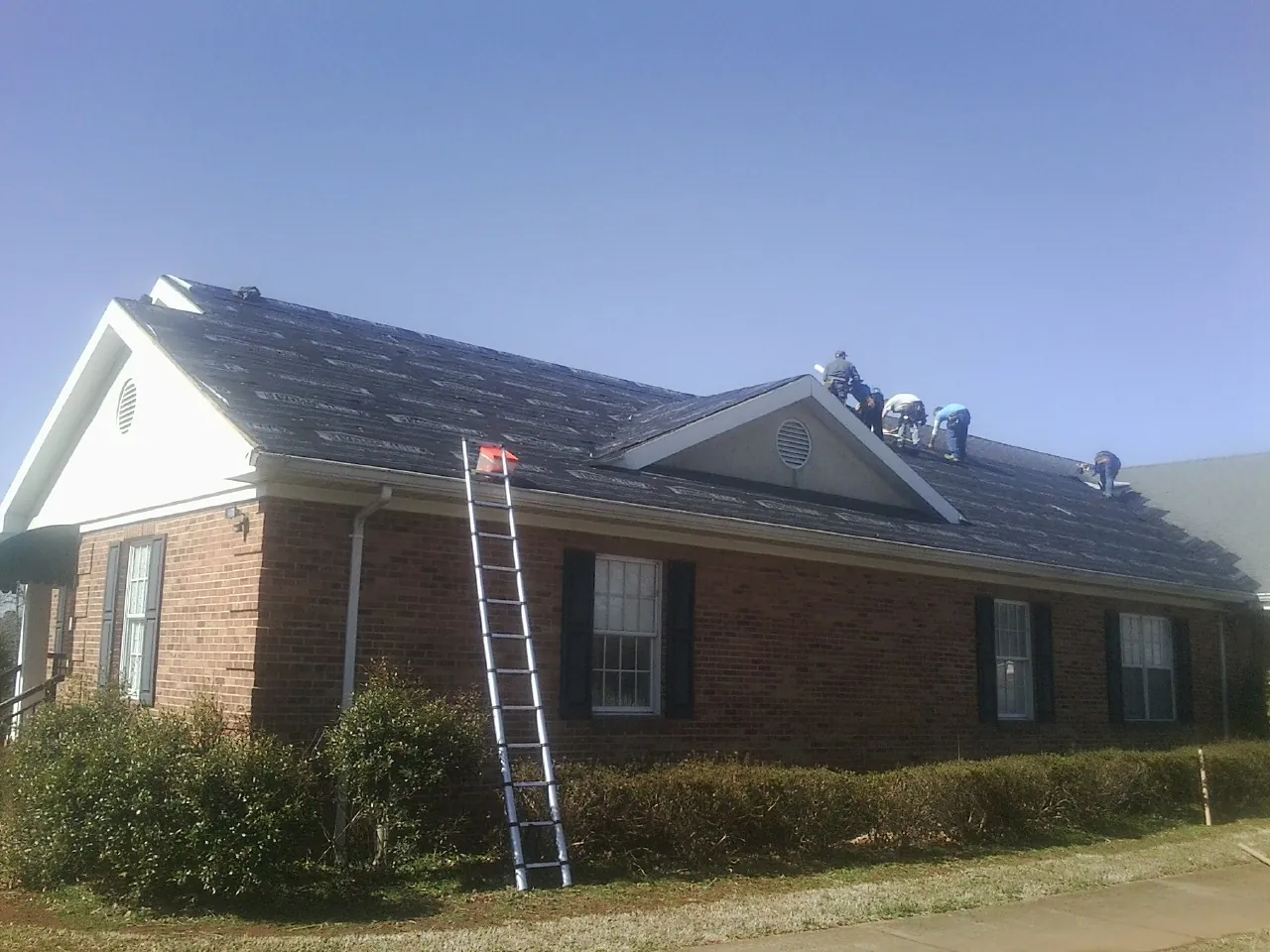 Crew tearing shingles off a brick ranch roof with a ladder set — Metal Roof Repair work by our crew in Saint James City