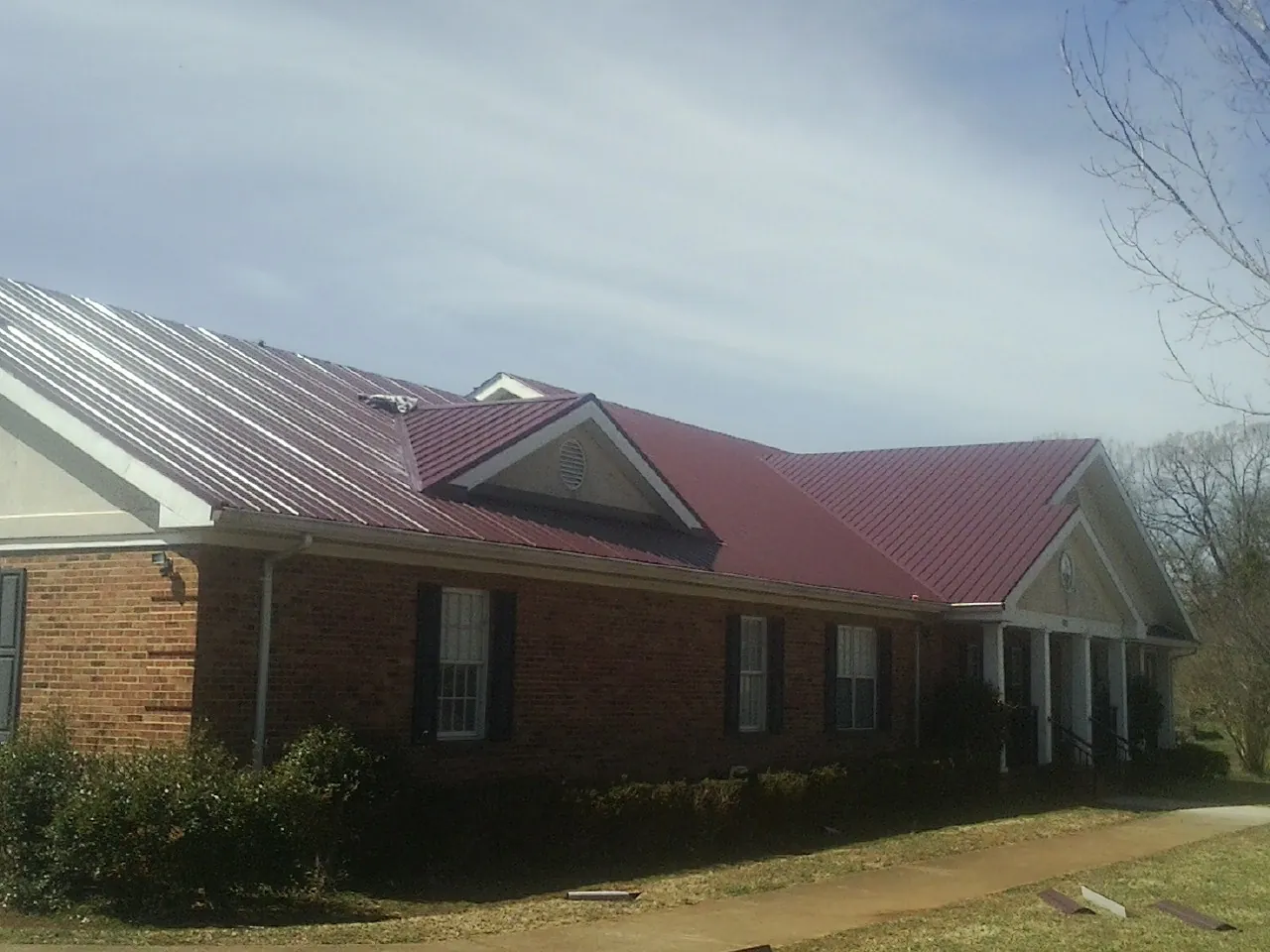 Red metal roof with gabled entries on a long brick building, from a Hail Damage Roof Repair job in Saint James City
