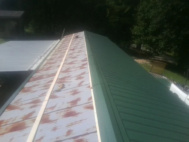 Old rusted panels beside newly installed green metal roofing — Wind Damage Roof Repair by Roofing Brothers in Saint James City