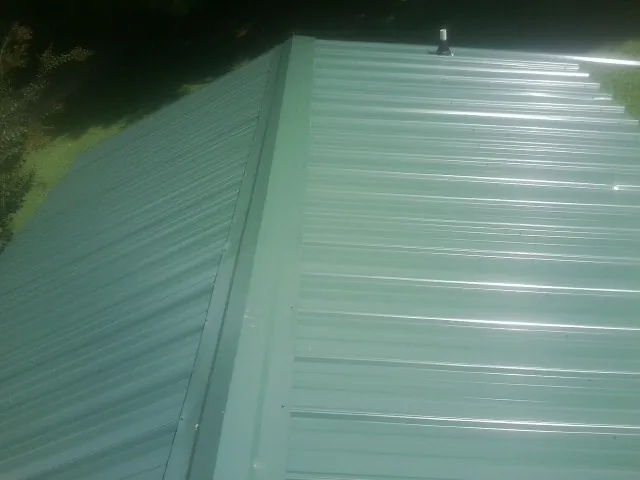 New green metal panels meeting at the ridge of a roof — Flat Roof Repair work by our crew in Saint James City