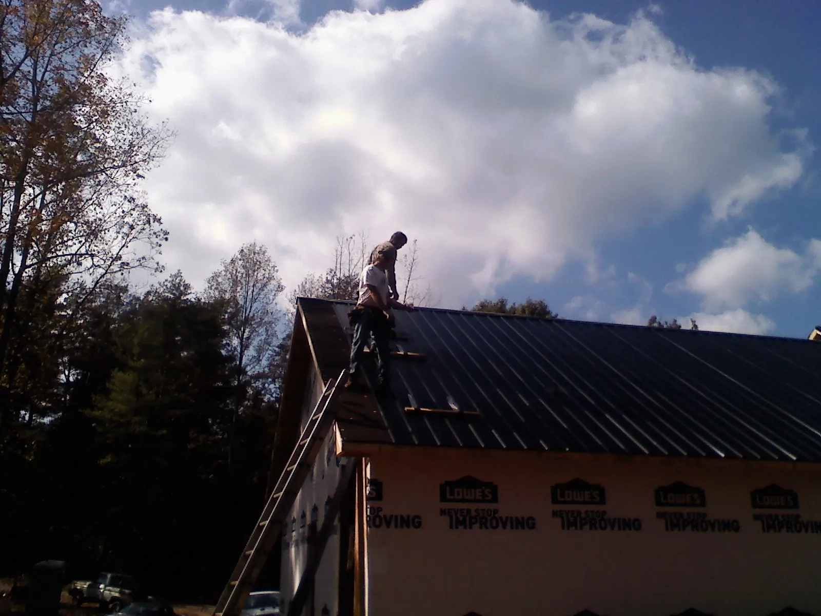 Roofer fastening dark metal panels high against a cloudy sky, from a Roof Inspection job in Saint James City